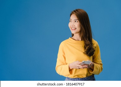 Young Asia lady using phone with positive expression, smiles broadly, dressed in casual clothing feeling happiness and standing isolated on blue background. Happy adorable glad woman rejoices success.