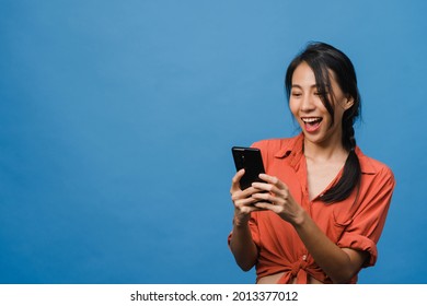 Young Asia Lady Using Phone With Positive Expression, Smiles Broadly, Dressed In Casual Clothing Feeling Happiness And Stand Isolated On Blue Background. Happy Adorable Glad Woman Rejoices Success.