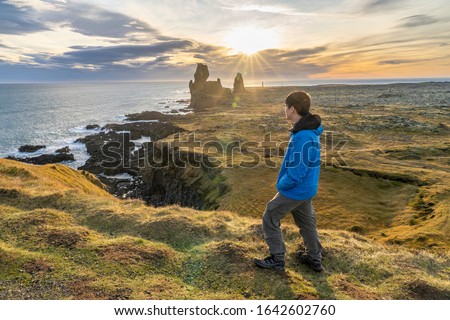 Young asia man standing to see sunset (Sunstar effect) in afternoon at volcanic rock  coast at  Londrangar famous cliffs in west iceland horizontal image