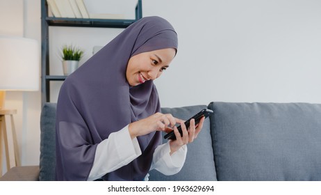 Young Asia Muslim Lady Use Smart Phone And Purchase E-commerce Internet On Sofa In Living Room At House. Stay At Home, Online Shopping, Self Isolation, Social Distance, Quarantine For Coronavirus.