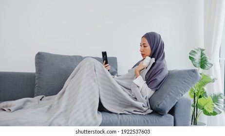 Young Asia muslim lady wear hijab using phone video call talking with doctor consultation or online consultation on sofa in living room at home. Social distancing, quarantine for coronavirus concept. - Powered by Shutterstock