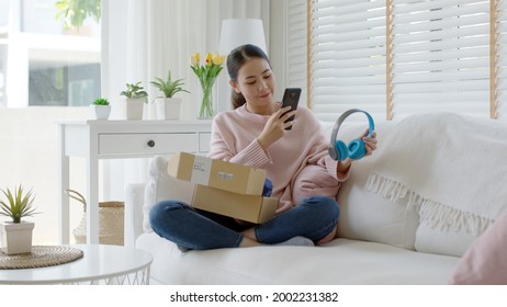 Young asia people happy teen girl smile unbox open gift new headphone buy order from online store shop take photo shoot camera show post social media app blog vlog share sit relax at home sofa couch.