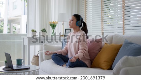 Young asia people teenage girl close eyes sit on sofa couch at home easy asana lotus pose in yoga app zen online class on internet on break time self relax calm, rest mind and mental health life care.
