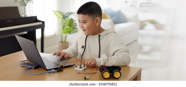 Young Asia Student Remotely Learn Online At Home In Coding Robot Car And Electronic Board Cable In STEM, STEAM, Mathematics Engineering Science Technology Computer Code In Robotics For Kids Concept.