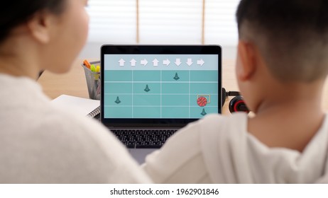 Young Asia Student Remotely Learn Online At Home With Parent In Coding Unplugged Coding Program On Laptop Computer For Beginner Kids. Self Study Parent Coach Teach Child In Basic Coding Language.