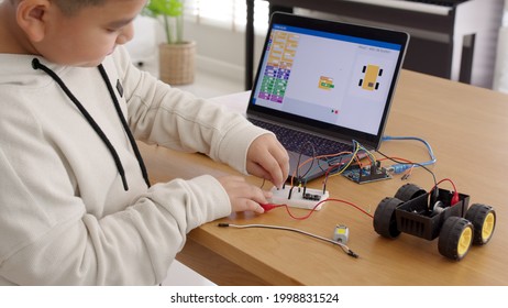 Young Asia Student Remotely Learn Online At Home In Coding Robot Car And Electronic Board Cable In STEM, STEAM, Mathematics Engineering Science Technology Computer Code In Robotics For Kids Concept.