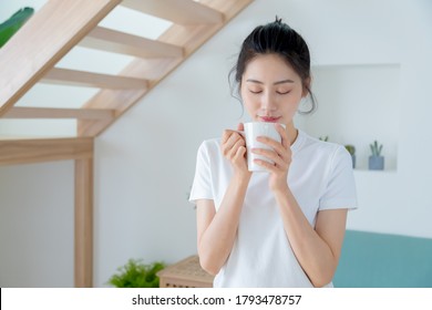 Young asia woman with ponytail in white t-shirt holding a cup of coffee or tea relaxing at home in the morning. - Powered by Shutterstock