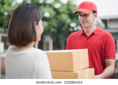 Young Asia Woman Receiving Parcel Cardboard Box From Post Man At Outdoor Of Home Which Smiling And Felling Happy, Delivery Man Express Shipping A Goods To Customer In Morning.