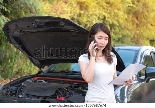Young asia woman\
sitting in front of her car, try to calling for assistance with her\
car broken down