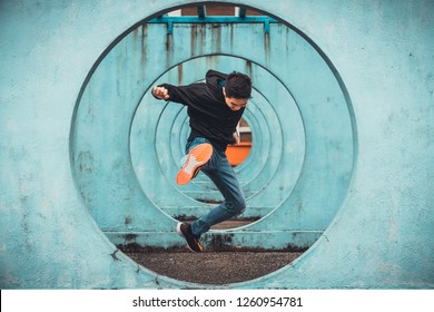 Young Asian Active Man Jumping And Kicking Action, Circle Looping Wall Background. Extreme Sport Activity, Parkour Outdoor Free Running, Or Healthy Lifestyle Concept