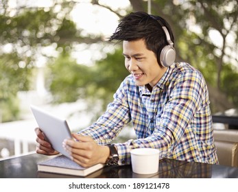 Young Asian Adult Man Wearing Headphone Using Tablet In Cafe.