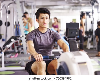 Young Asian Adult Man Working Out In Gym Using Rowing Machine.