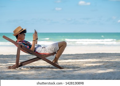 Young asian adult men traveler in casual wear relaxing and lying down on beach chair on tropical island beach in summer holidays vacation travel trip using smartphone for text, selfie or take a photo - Powered by Shutterstock