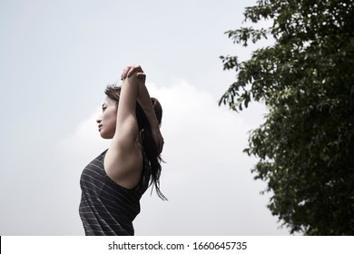 young asian adult woman stretching arms outdoors, low angle side view