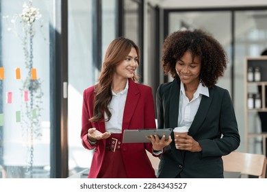 Young Asian and African businesswoman African woman relaxing with coffee mug while brainstorming investment plan Financial business together in the office management concept. - Powered by Shutterstock