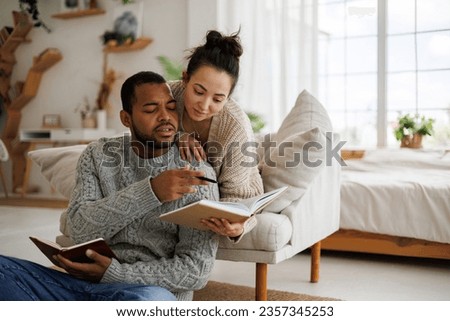 Young asian american man in sweater holding notebook near asian girlfriend and book at home