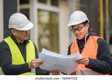 Young Asian apprentice at work on construction site with senior engineer. Outdoors