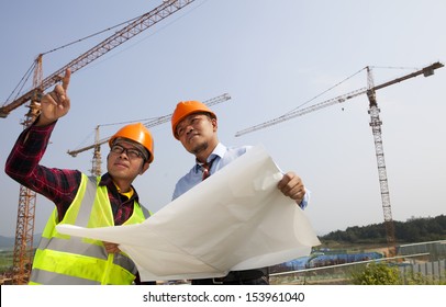 Young Asian Architects Discussion At Blueprint In Front Of Construction Site, Horizontal Image