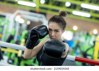 Young asian athlete woman posing in boxing gloves, Female boxer hitting a huge punching bag at a boxing studio. Woman boxer training hard, Attractive Asian Female Boxer At Training.