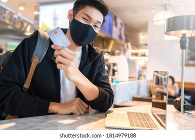 young asian attractive male traveller wearing facial mask virus protection hand hold credit card for shopping online with laptop at cafe restaurant business ideas new normal lifestyle - Powered by Shutterstock