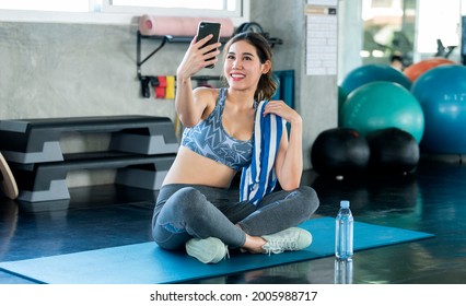 Young Asian Attractive Smiling Active Fitness Sitting On The Floor Of The Gym And Taking A Selfie.