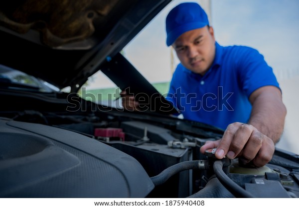 A young Asian auto mechanic opens the bonnet. To\
check for engine damage And perform professional maintenance. He\
wearing blue uniform.