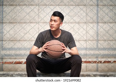 Young Asian Basketball Player Holding A Ball Sitting Resting At Courtside