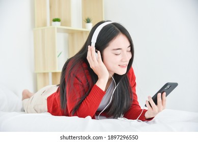 Young Asian Beautiful Girl Lying On Bed And Listen Music From Smart Phone Via Headphone.