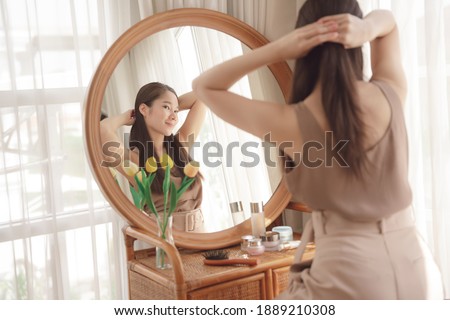Young asian beauty woman tying her hair infront of rounded mirror.