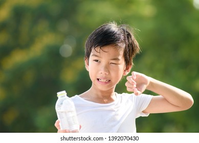 Young Asian Boy Carry A Bottle Of Water And Feel Hot In A Summer Day In A Park