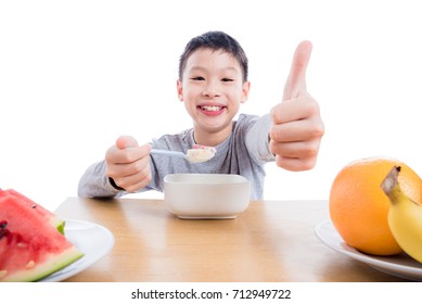 Young asian boy eating cereal with yogurt and fruit for breakfast over white background