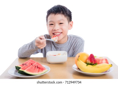 Young Asian Boy Eating Cereal With Yogurt And Fruit For Breakfast Over White Background