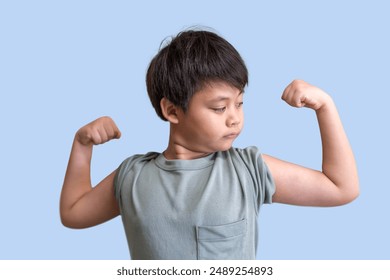 Young asian boy flexing his muscles against a light blue background showcases strong and poses with both arms flexed, childhood strength and determination, empowerment, confidence, fitness and health - Powered by Shutterstock