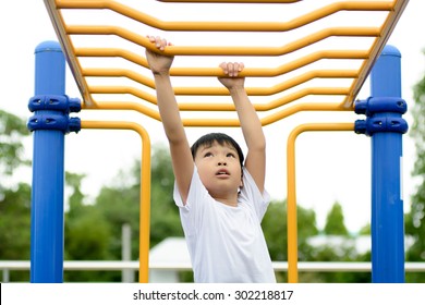 Young asian boy hang the yellow bar by his hand to exercise at out door playground - Powered by Shutterstock