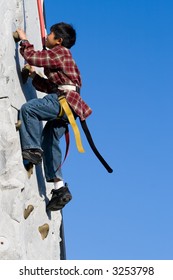 Young Asian Boy Outside Climbing On A Rock Climbing Wall With Clear Blue Sky In Background