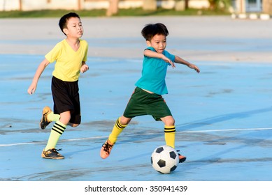 Young Asian Boy Play Football On The Blue Concrete Floor During Summer.