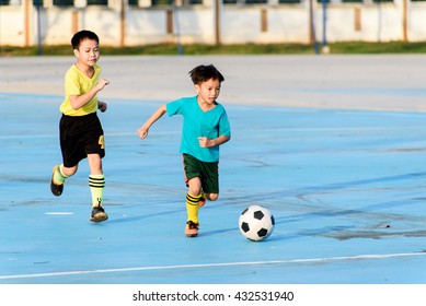 Young Asian Boy Play Football On The Blue Concrete Floor During Summer.