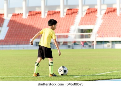 Young Asian Boy Play On The Grass Football Field In The Stadium During Summer.