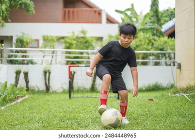 Young asian boy playing soccer with the soccer ball in garden, child joy and energy of outdoor play, childhood, kids, soccer, sports and exercise, sportsmanship and importance of physical activity - Powered by Shutterstock