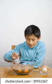 young Asian boy pouring cooking oil into bowl of cake batter