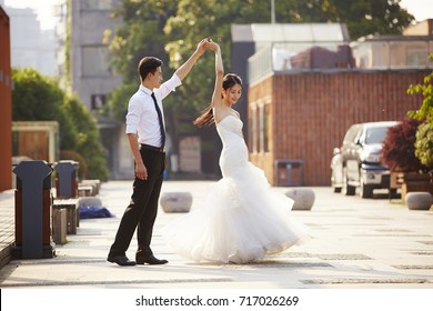 young asian bride and groom in wedding dress dancing in parking lot.
