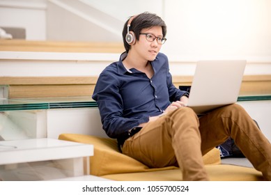 Young Asian Business Man Enjoy Watching Movie Online With Laptop Computer On Ths Stair In Living Space. Relaxing Urban Lifestyle In Accommodation Concepts