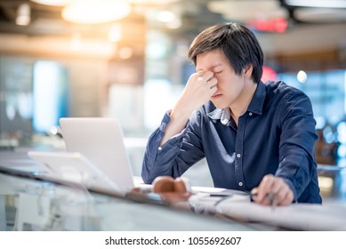 Young Asian Business Man Feeling Stressed And Frustrated While Working With Laptop Computer. Male Entrepreneur Getting In Trouble With His Job. Freelance Lifestyle In Urban Workspace.