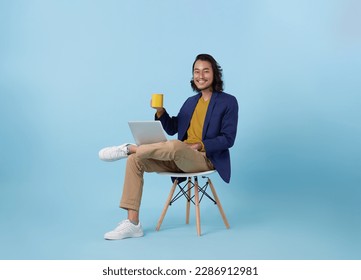 Young asian business man happy smiling using computer laptop sitting on white chair and drinking coffee isolated on blue studio background. - Powered by Shutterstock