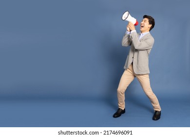 Young Asian Business Man Holding Megaphone Isolated On Blue Background, Speaker And Announce Concept, Full Body Composition