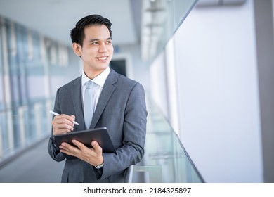 Young asian business man holding a tablet looking away , smart business concept. - Powered by Shutterstock