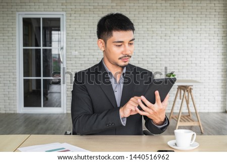 A young Asian business man siting looking and working on his tablet in the office.