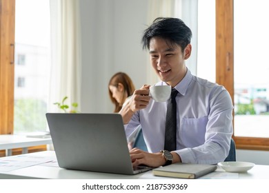 Young Asian Business Man Working With Laptop, Tablet And Papers On Desk At Office. He Feeling Good And Happy.