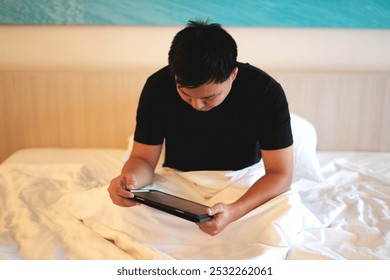 Young asian business man working on a business trip video calling his colleague and working with tablet while relaxing on bed in a luxury hotel room and this is a travel and business concept. - Powered by Shutterstock