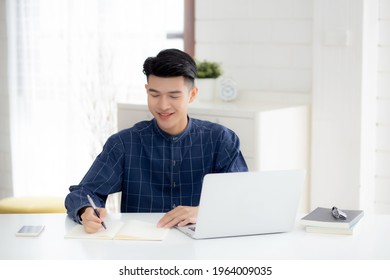 Young Asian Business Man Writing On Notebook For Planning Working And Using Laptop Computer On Desk At Home, Notes About Finance, Male Study And Learning, Business And Communication Concept.